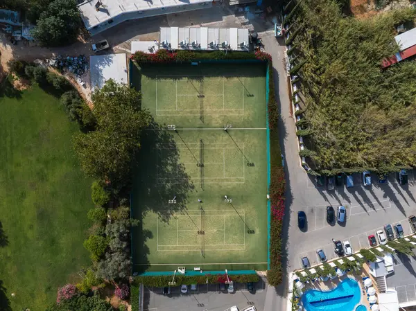 Kıbrıs Rum Kesimi 'nin Ayia Napa kentindeki bir tatil köyünde havadan çekilmiş dört çimen tenis kortu, mavi bir havuz, park alanı ve yemyeşil alan görüntüsü.
