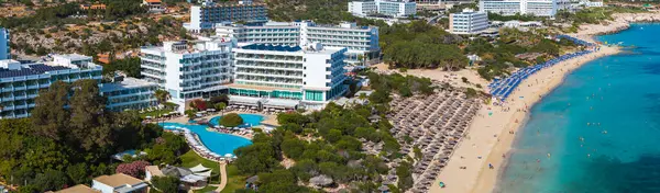 Kıbrıs Rum Kesimi 'nin Ayia Napa kentinin hava manzarası, lüks tatil beldelerini, güneşli kumsalları, turkuaz Akdeniz sularını ve yemyeşil alanları gösteriyor..