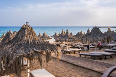 Kıbrıs 'ta sazdan yapılmış şemsiyeler, tahta güneşlikler, ahşap bir yürüyüş yolu, altın kum ve turkuaz Akdeniz suları olan sakin bir sahil..
