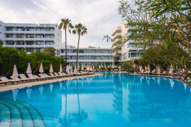 Kıbrıs 'ta geniş bir havuzu, beyaz şemsiyeleri, şezlongları, uzun palmiye ağaçları ve bereketli yeşillikleri olan modern bir otel tesisi huzur verici bir ortam yaratıyor..