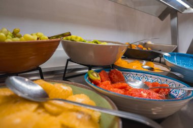 Canlı bir açık büfede üzüm, kivi, çilek ve turunçgiller renkli kâselerde metalik bir tezgahta kaşıklarla servis edilen taze meyveler bulunur..