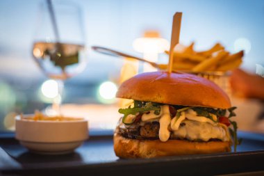 Peynirli ve yeşillikli bir gurme hamburgerin kapağı metal bir sepet, sos ve sıcak bir akşamda bir bardak beyaz şarap ile servis edilir..