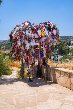Rengârenk kurdelelerle süslenmiş kalp şeklinde bir yapı ve Kıbrıs 'taki dağlık bir Akdeniz manzarasına karşı döşenmiş asfalt bir yolda notlar..