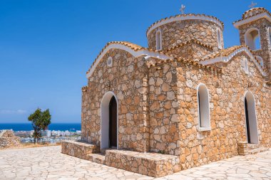 Geleneksel Bizans taşı St. Elias Kilisesi kemerli pencereleri, kubbesi ve çan kulesi olan bir tepede. Arka planda kıyı kasabası ve Akdeniz görünüyor.