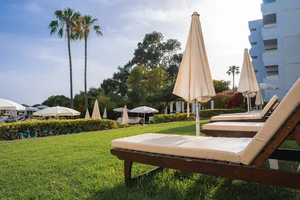 Kıbrıs 'ta ahşap şezlonglar, krem yastıklar, şemsiyeler, uzun palmiye ağaçları ve modern beyaz bir binası olan lüks bir otelin açık hava bölgesi..