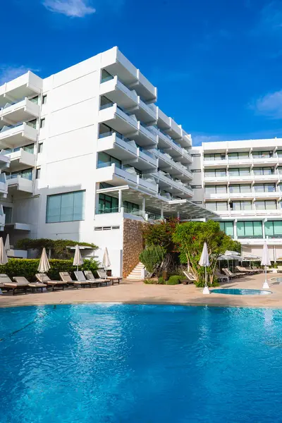 Kıbrıs 'ta balkonları, el değmemiş bir havuzu, şezlongları, şemsiyeleri, yemyeşil ve parlak mavi gökyüzü olan modern beyaz çok katlı bir otel..