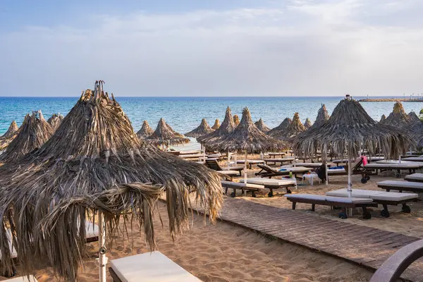 Kıbrıs 'ta sazdan yapılmış şemsiyeler, tahta güneşlikler, ahşap bir yürüyüş yolu, altın kum ve turkuaz Akdeniz suları olan sakin bir sahil..