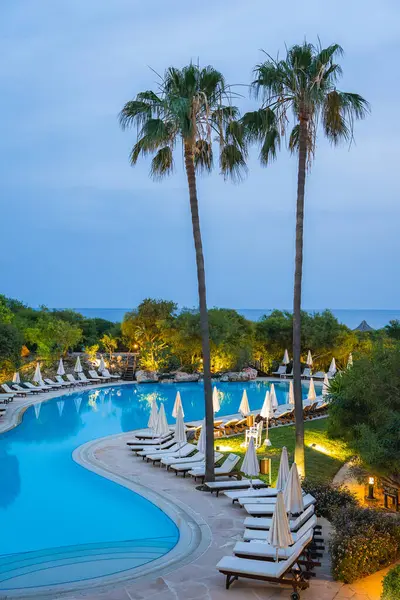 Kıbrıs 'ta, yüksek palmiye ağaçları, beyaz şezlonglar ve şemsiyelerle çerçevelenmiş, yemyeşil ve bulutlu gökyüzü altında deniz manzaralı sakin bir tatil köyü..