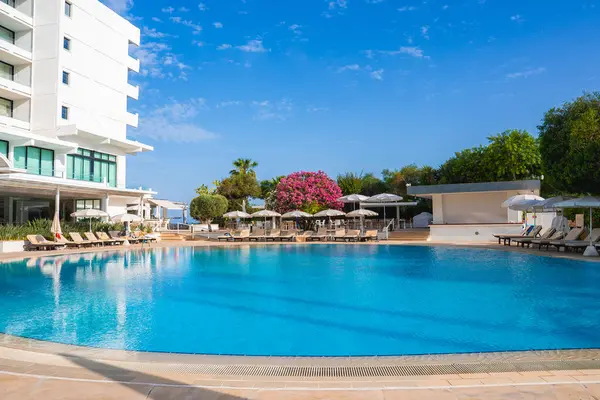 Kıbrıs 'ta el değmemiş bir havuzu, güneş pansiyonları, şemsiyeleri, pembe begonvilleri, yemyeşil bir oteli ve arka planda açık mavi bir gökyüzü olan modern bir otel..