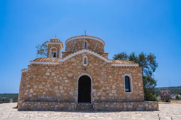 Geleneksel Bizans tarzı taş Aziz Elias Kilisesi. Kubbesi ve kemerli pencereleri, solunda çan kulesi ve parlak mavi gökyüzünün altında asfalt bir avlusu var..