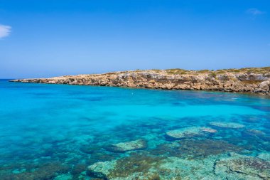 Su altı kayalarıyla kristal berrak turkuaz sular, sakin Kıbrıs kıyı manzarası altında engebeli ve kayalık bir kıyı şeridiyle kesişiyor..