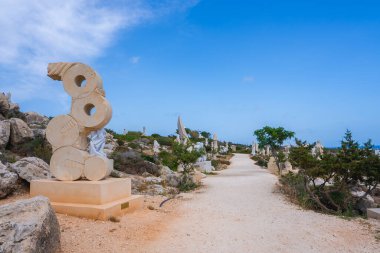 Kıbrıs 'taki bir heykel parkında soyut taş heykellerle dolu bir patika bulunuyor. Kurak arazi kayaları, çalıları ve açık bir gökyüzünün altındaki ağaçları içerir..