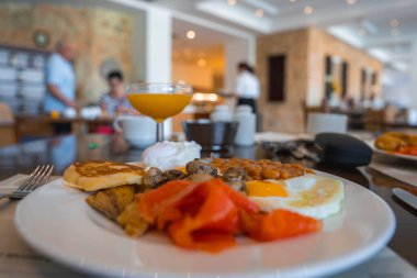 Tütsülenmiş somon, yumurta, fasulye, mantar ve daha fazlası ile canlı bir kahvaltı tabağı, taş dokulu duvarları olan modern bir yemek alanında..