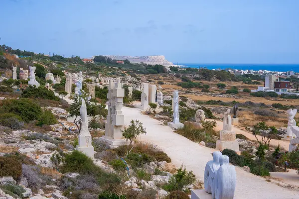 Kıbrıs 'ta, seyrek bitki örtüsü, deniz manzarası ve kıyı kasabası manzaralı kayalık bir arazide, patika boyunca uzanan beyaz taş heykellerin yer aldığı bir heykel parkı..