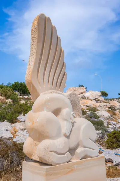 Kanatlı bir atın kayalık araziye, seyrek bitki örtüsüne ve Kıbrıs 'ta parlak mavi gökyüzüne dayanan kaidedeki ayrıntılı taş heykeli..