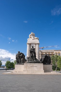 Budapeşte 'deki Tisza Istvan Anıtı' nda, turna ve tarihi bina ile mavi gökyüzüne karşı dizilmiş bronz heykeller ve merkezi bir heykel yer alıyor..