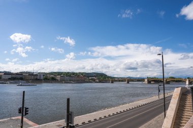 Tuna Nehri Budapeşte, Macaristan 'dan geçer, arkada bir köprü, solda binalar ve önünde merdiven olan bir yol bulunur..