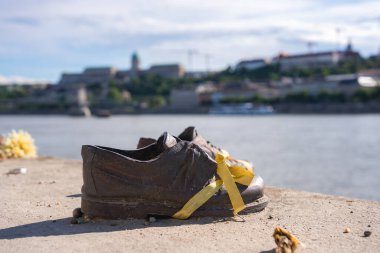 Budapeşte, Macaristan 'daki Danube Bank Anıtı' ndaki ayakkabılar, bronz ayakkabılar, sarı kurdeleler ve bulutlu bir gökyüzünün altında görünen Buda Kalesi..