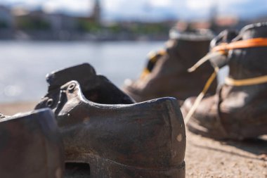 Budapeşte 'deki Tuna Nehri' nin arkasında bulanık şehir manzarası ve su bulunan Yahudi Soykırımı anıtının bronz ayakkabıları..