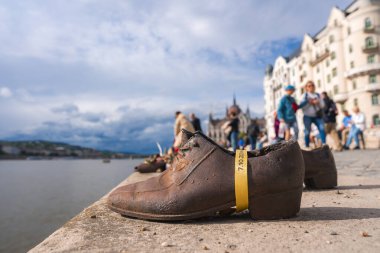 Macaristan 'ın Budapeşte kentindeki Tuna Nehri kıyısında paslı demir ayakkabılar hizalanırken, Macar Parlamentosu binası bulutlu bir gökyüzünün altında görülebiliyor..