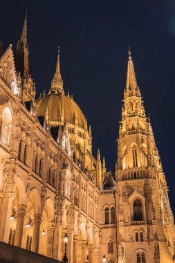 Budapeşte 'deki Macar Parlamento Binası geceleri sıcak bir şekilde parlıyor. Neo Gotik mimarisini kuleler, kemerli pencereler ve merkezi bir kubbeyle sergiliyor..