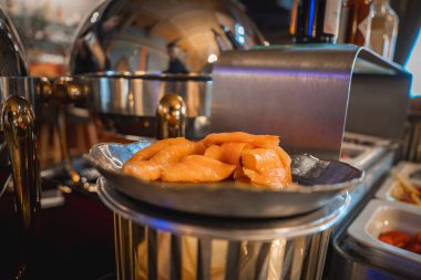 Metalik bir tepside ince ince dilimlenmiş füme somon tabağı, sıcak, zarif bir yemek ortamında cilalanmış gümüş aşındırıcı tabaklarla çevrili..