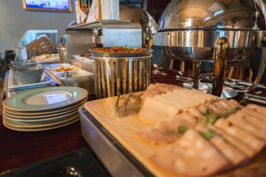 Ahşap bir tahtanın üzerinde soğuk pirzola, gümüş aşındırıcı tabaklar, istiflenmiş tabaklar, sıcak ışıklandırma ve bir butik otelin rafine dekoru olan lüks bir büfe..