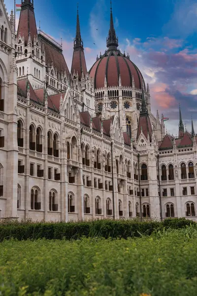 Macaristan 'ın Budapeşte kentindeki Macar Parlamento Binası' nda Neo Gotik mimari, merkezi bir kubbe, kuleler, bir bahçe ve mavi bir gökyüzü yer alıyor..