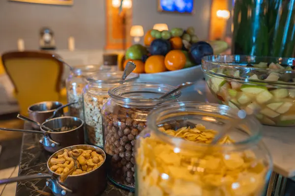 Cam kavanozlu mermer tezgah, taze meyve salatası ve dekoratif meyve tabağı. Sarı sandalye ve yumuşak ışıklandırma rahat atmosferi güçlendirir.