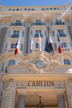 Fransa 'nın Cannes kentindeki Carlton Oteli' nde dekoratif sütunlar, balkonlar, merkezi bir saat ve belirgin bir şekilde sergilenen bayraklar yer alıyor..