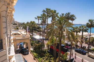 Cannes, Fransa 'daki Carlton Oteli manzarası, arka planda palmiye kaplı caddeler, lüks arabalar, festival tabelası ve Akdeniz.