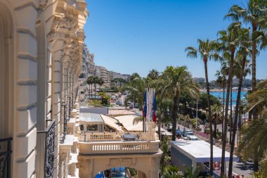 Carlton Oteli 'nin dekoratif mimarisi solda duruyor. Sokakları palmiye ağaçları kaplıyor ve arka planda Akdeniz görünüyor..