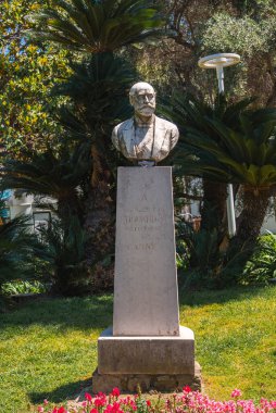 Mösyö Le Fol Gouraud 'nun Cannes, Fransa' da bir bahçede, taştan bir heykel üzerinde büstü. Palmiye ağaçları, çiçek açan bitkiler ve bir sokak lambası ile çevrili..