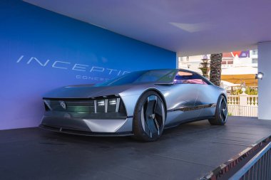 Açısal tasarımı ve büyük tekerlekleri olan parlak metalik bir konsept araba. Cannes, Fransa 'da palmiye ağaçları ve bir bina görülebilir..