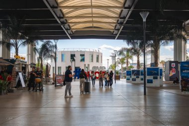 Nice Cote d 'Azur Havalimanı' ndaki kıvrımlı bir tepenin altında, palmiye ağaçları, gezginler ve arka planda dairesel bir bina var..