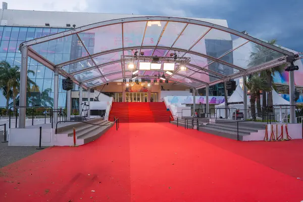 İkonik kırmızı halı, Fransa 'nın Cannes kentindeki Palais des Festivals et des Congres' e, cam bir cephe, palmiye ağaçları ve bulutlu bir gökyüzüne götürür..