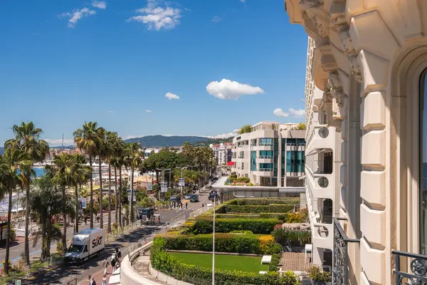 Cannes, Fransa 'da canlı bir cadde, Carlton Hotel cephesi, palmiye çizgili gezinti güvertesi, modern binalar, ve mavi gökyüzünün altında Akdeniz.