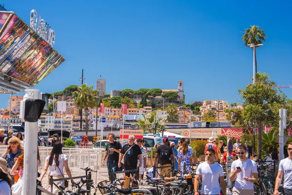 Fransa 'nın Cannes şehrinde bisikletli bir kalabalık, Le Suquet' nin saat kulesi ve parlak mavi gökyüzü ve palmiye ağaçlarının altındaki bir tepede ortaçağ mimarisi.