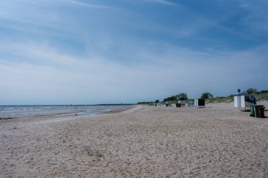 A tranquil beach in Parnu, Estonia, featuring calm waters, a clear blue sky, colorful kites in the distance, and a small structure on the left.
