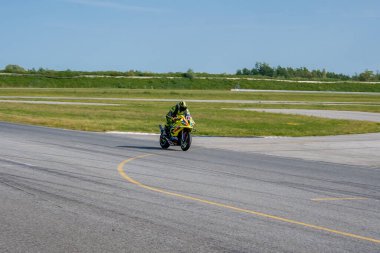 Sarı ve siyah kıyafetli bir motosikletçi Porsche pistinin virajında, çimenler, ağaçlar ve açık mavi gökyüzü ile çevrili bir spor bisikletine biniyor..