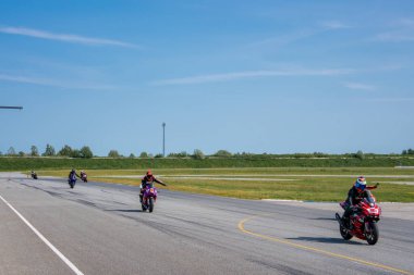 Çimlerle çevrili profesyonel bir pistte bisiklet yarışçıları grubu. Kırmızı bir bisiklet önden, diğerleri arkadan takip ediyor..