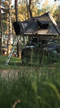Siyah bir BMW X4 SUV, Ikamper 'ın çatısı olan bir çadırda park halinde. Çadır, yüksek ağaçlarla çevrili metal bir merdivenle dolu..