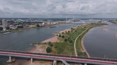 Hollanda, Nijmegen 'in hava görüntüsü, Waal Nehri, De Oversteek köprüsü, hareket eden su, araçlar, rüzgar türbinleri ve kentsel manzaraları gösteriyor..