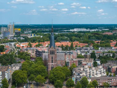Hollanda 'nın Eindhoven kentinin havadan görünüşü, yüksek bir kilise, kırmızı kiremitli çatılar, modern binalar, yeşil ağaçlar ve mavi gökyüzünün altında düz bir ufuk..