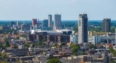 Hollanda, Eindhoven 'ın hava manzarası, açık mavi gökyüzü altında Philips Stadyumu, modern kuleler, geleneksel binalar ve yeşillik.