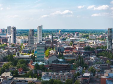 Eindhoven, Hollanda 'nın havadan görünüşü, modern eğri kuleleri, bir kilise kulesini, yeşil alanları ve mavi gökyüzünün altında bulutlu düz bir ufku gösteriyor..