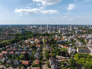 Hollanda 'nın Eindhoven kentinin havadan görünüşü, açık mavi gökyüzü altında ağaç kaplı sokakları, kırmızı fayanslı evleri, modern yüksek binaları ve yeşillikleri gösteriyor..