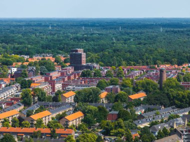 Hollanda 'nın Eindhoven kentinin havadan görünüşü turuncu kiremitli çatılar, silindirik tuğla bir kule, yeşil ağaçlar, açık alanlar ve arka planda bir orman gösteriyor..