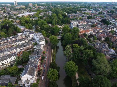 Hollanda 'nın Utrecht kentinin hava manzarasında merkezi bir kanal, yemyeşil ağaçlar, tarihi Hollanda binaları, park edilmiş arabalar ve caddeler boyunca bisikletler yer alıyor..