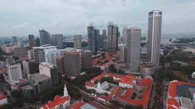 Singapur 'un gökdelenlerini gösteren hava manzarası, modern gökdelenler, kırmızı çatılı binalar, Marina Bay Sands, Swissotel Stamford, ve yemyeşil.